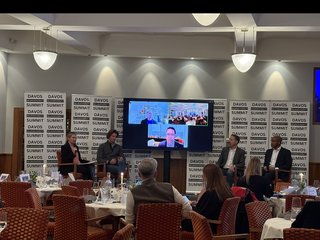 A DNS panel discussion on stage, with remote panelists joining by video.
