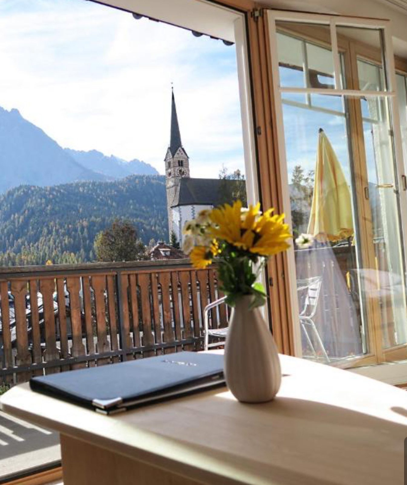View from a Davos hotel balcony over a wooden railing toward a church spire and snow-capped mountains