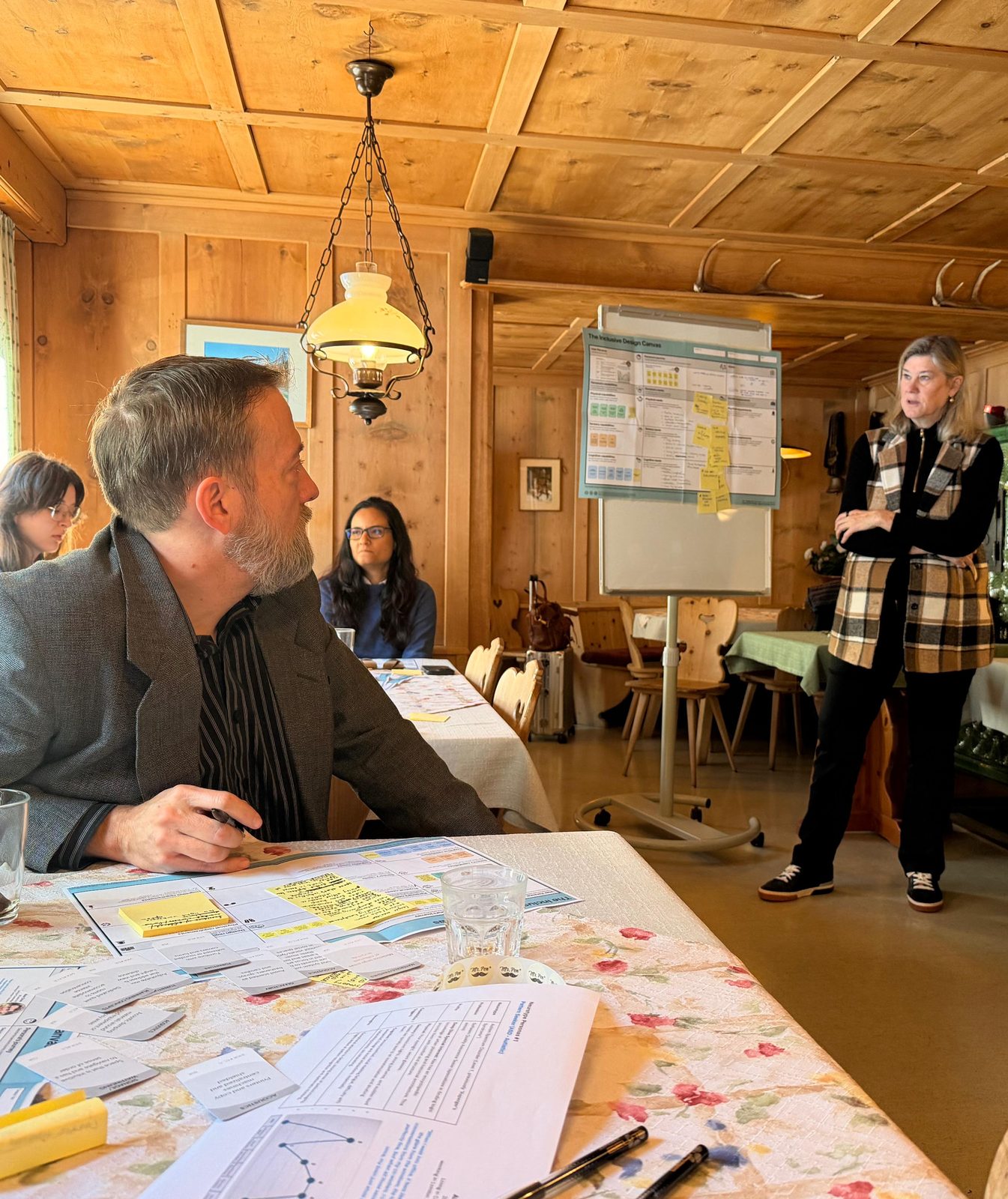 Small-group workshop session in a wood-panelled Alpine cabin, participants reviewing an inclusive design canvas