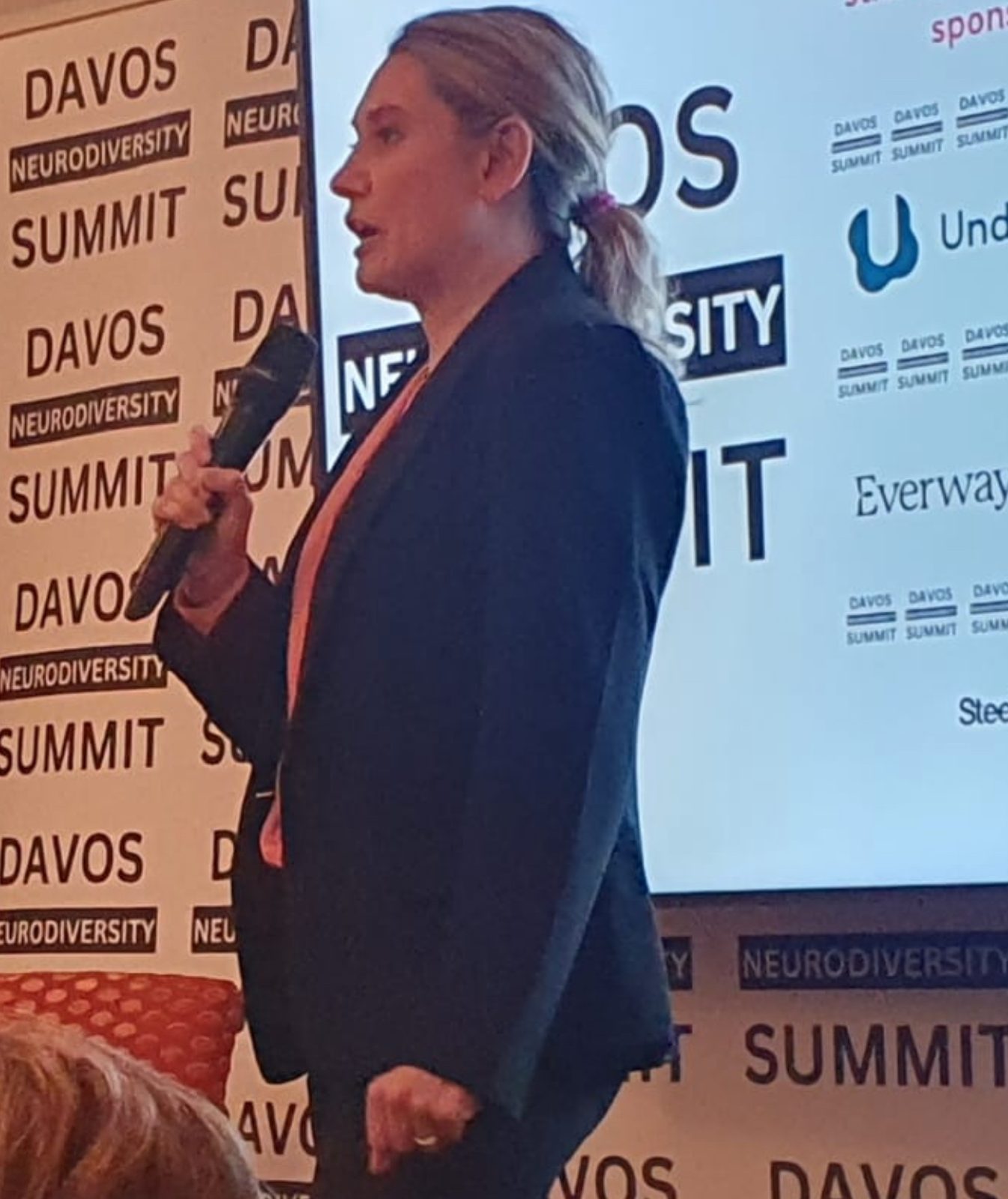 Speaker addressing the audience at DNS, holding a microphone in front of a Davos Neurodiversity Summit backdrop