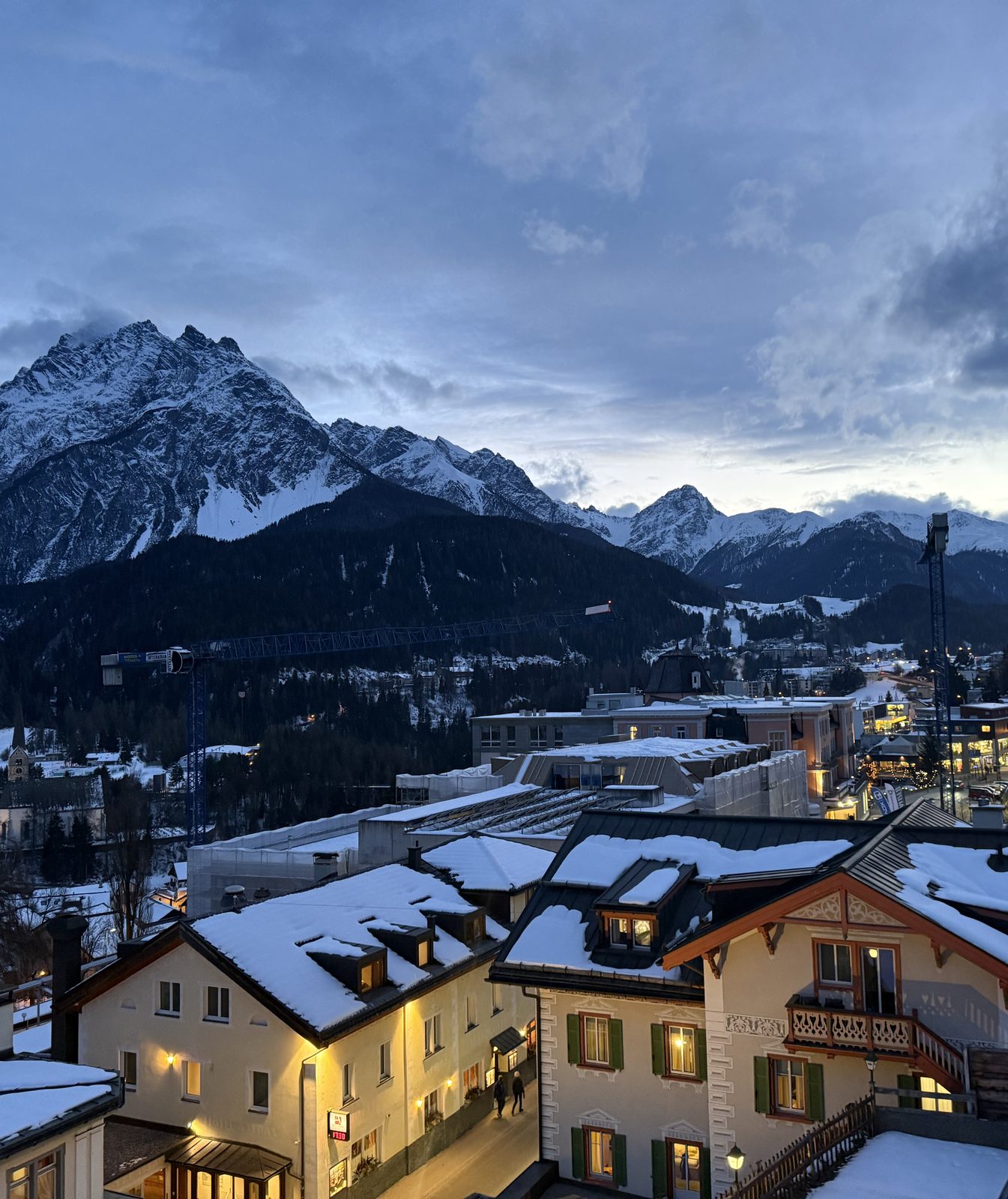 Snow-covered mountain peaks above the town of Davos at dusk, chalet rooftops lit from within